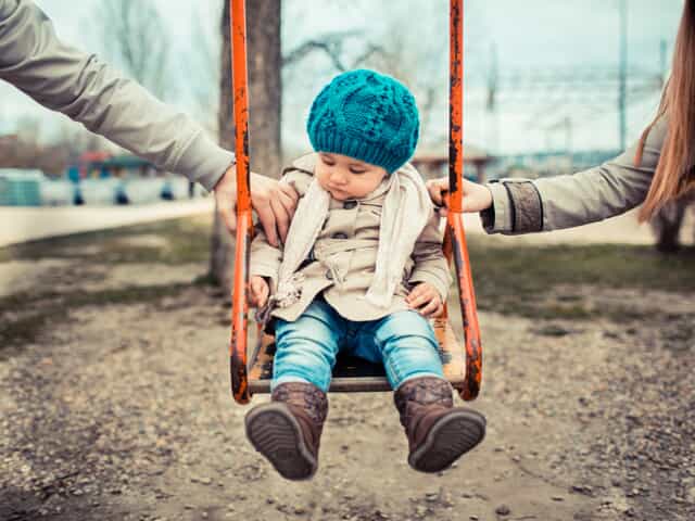parents both holding on to child on swing wearing beanie